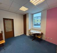 Offices with a blue carpet, pink wall, window, and a table with chairs.