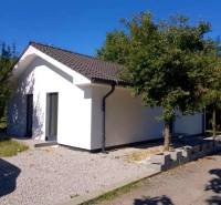 A family house in Kaplna with a white facade, a sloped roof, and greenery around.