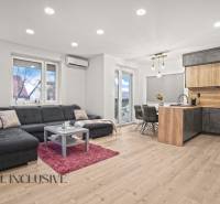 Living room with a kitchenette, gray sofa, wooden decor flooring, dining table.