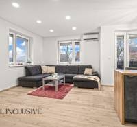 Living room of a three-room apartment with a wooden decor floor, comfortable seating, and large windows.