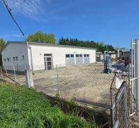 Warehouses and halls in Šaľa, a white building with a gate and fencing, surrounded by greenery.