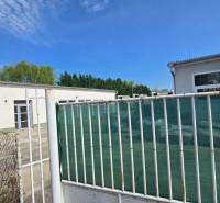 The white building in Šaľa is part of Warehouses and Halls, surrounded by a fence and greenery.