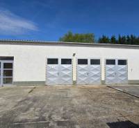 A white building with four metal gates and an entrance in Šaľa, suitable for warehouses and halls.