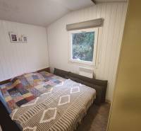 Bright bedroom in a cottage with a bed, window, and wooden wall paneling.