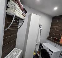 A bathroom in a 3-room apartment with a washing machine, shelves, and a wooden decor floor.