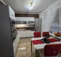 A kitchen in a 3-room apartment with glossy white cabinets, appliances, and a dining table.