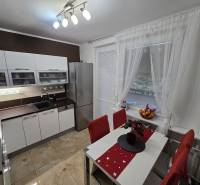 A kitchen in a 3-room apartment with white furniture, a dining table, and a floor with a wood decor.