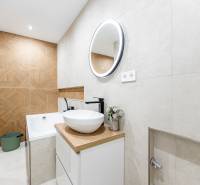 Bathroom of a two-room apartment with light tiles and a wooden decor floor.