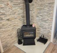 A wood-burning fireplace in the corner of the room with stone cladding and a wooden decor floor.