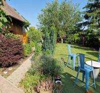 The garden of a family house in Dlhá nad Váhom with a wooden cottage and blue chairs.