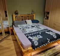 A bedroom in a family house with a wooden bed, built-in wardrobes, and a floor with a wooden decor.