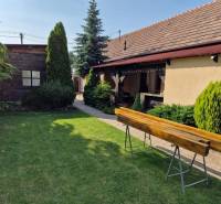 A family house in Dlhá nad Váhom with a lawn, bushes, and a wooden bench in the garden.