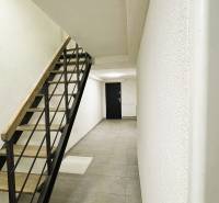 A hallway of a family house with minimalist stairs, light walls, and tiles.