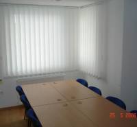 Commercial space with a conference table, blue chairs, and vertical blinds.
