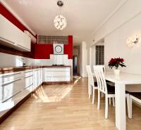 A kitchen in a 2-room apartment with white furniture and a wooden decor floor.
