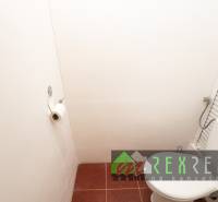 A toilet in a 4-room apartment with white walls and red tiles.