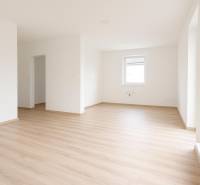 White interior of a family house with a wood-patterned floor and a large window.