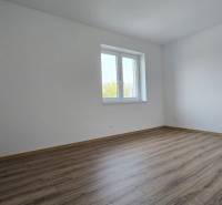 An empty room in a family house with a wood-patterned floor and a window.