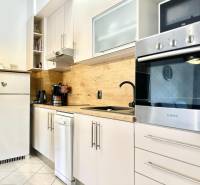 A kitchen in a vacation apartment with white furniture and wooden decor on the wall.