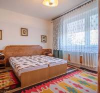 Bedroom in a family house with a bed, carpets, and curtains on the window.
