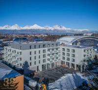 A building in Poprad with the snow-covered Tatras in the background and an ice rink.