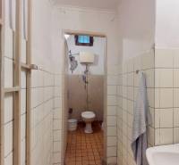 A bathroom with a sink, towel, and toilet with older tiles in commercial premises.