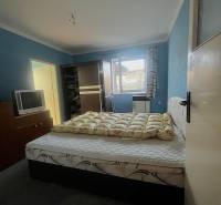 Bedroom with a bed, dark wardrobe, television, and blue walls in a family house.