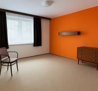 A room with an orange wall, furniture, a window, and carpeted flooring in a family house.
