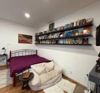 Bedroom in a one-room apartment with a bed, bookshelf, and wooden decor flooring.