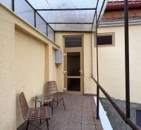 A covered patio with two chairs and a table in front of the entrance to a studio apartment.