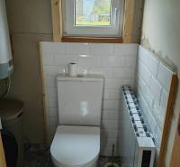 A toilet with white tiles and a view through a small window in a family house.