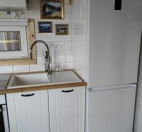 A kitchen in a family house with white cabinets, a refrigerator, and artistic paintings on the wall.