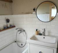 A bathroom in a family house with a bathtub, white tiles, and a round mirror.