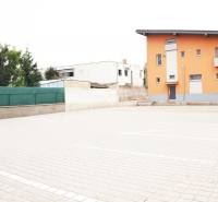 Orange building in Šaľa with a steep roof and a paved parking area.