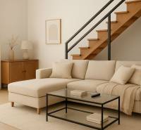 Interior of a building with a beige sofa, staircase, and wood-patterned flooring.