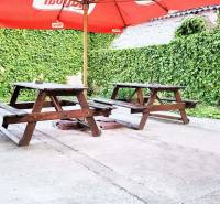 Garden terrace in Šaľa with wooden tables and chairs under a red umbrella.