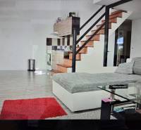 Living room with a kitchenette, staircase, sofa, glass table, and wooden decor flooring.