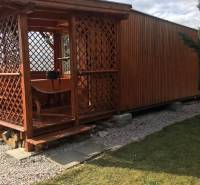 A wooden cottage in Kráľová nad Váhom with a small raised terrace and a lawn.