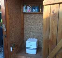 Wooden cabin in Kráľová nad Váhom with a chemical toilet and a shelf.