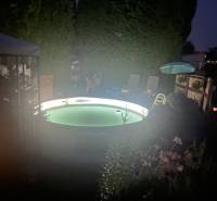 A night garden by the cottage in Kráľová nad Váhom with a lit pool and loungers.