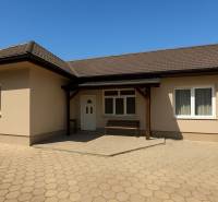 A family house in Tešedíkovo with a sloped roof, paving, and a wooden shelter.