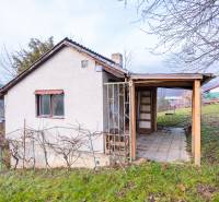 A cottage in Prešov with a wooden structure and a vineyard on a grassy hill.