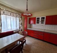 A kitchen in a family house with red kitchen cabinets and white curtains.
