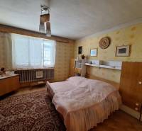 A bedroom in a family house with retro furniture, a carpet, and yellow wallpaper.