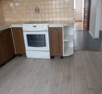 A kitchen with brown cabinets, a white stove, and a floor with a wood design, in a three-room apartment.