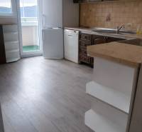A kitchen in a 3-room apartment with a wooden decor floor, a white refrigerator, and a dishwasher.