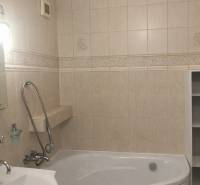 The bathroom of a three-room apartment with a bathtub and beige wall tiles.