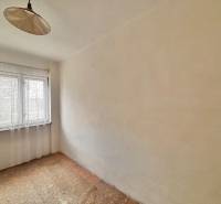 A room in a family house with one window and a curtain, with carpeted flooring.