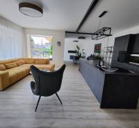 Living room with a large sofa and a modern kitchen, floor with wooden decor.