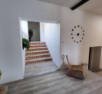 Interior of a family house with a clock on the wall, a floor with a wooden design, and stairs with a colorful pattern.